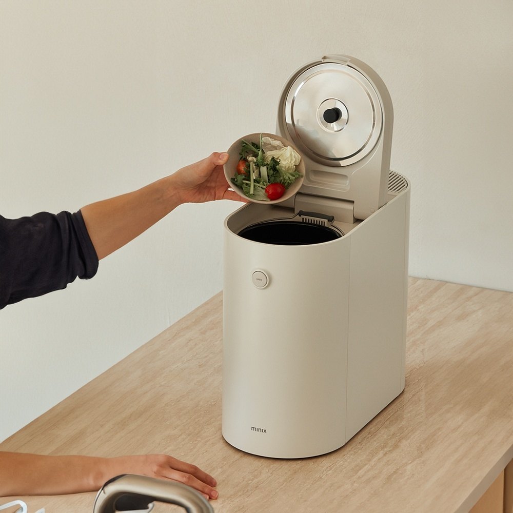 Hand scraping vegetable scraps from a bowl into the open Minix Plender PRO