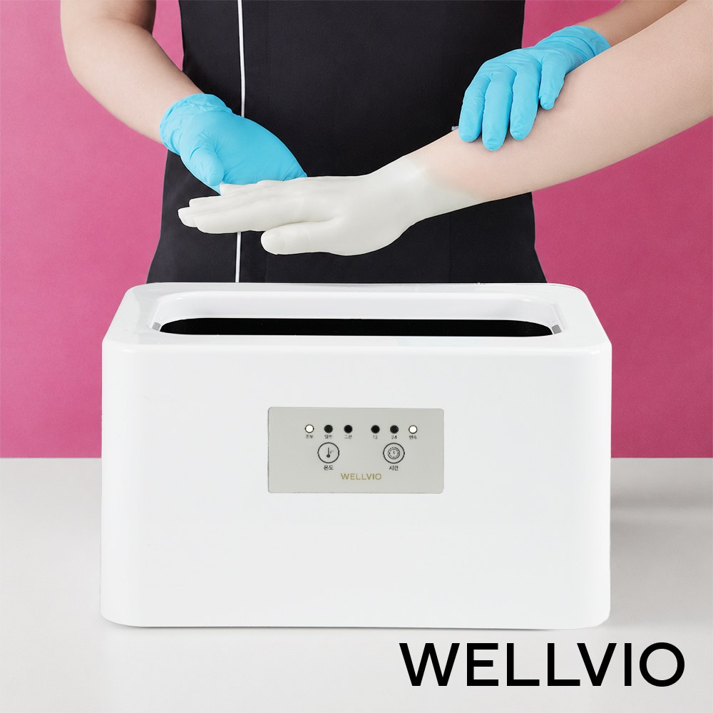 Hand peeling off a paraffin wax coating above the white Wellbio Classic Paraffin Bath tub